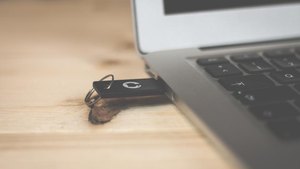 A small black key fob lying on a wooden desk beside the edge of a laptop