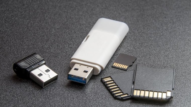 Two USB flash drives and three memory cards laid out on a dark grey surface
