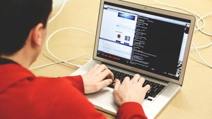 A person in a red sweater typing on a laptop with a dark code editor open