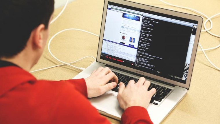 A person in a red sweater typing on a laptop with a dark code editor open