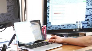 Hands typing on a laptop on an office desk, a larger external monitor behind it
