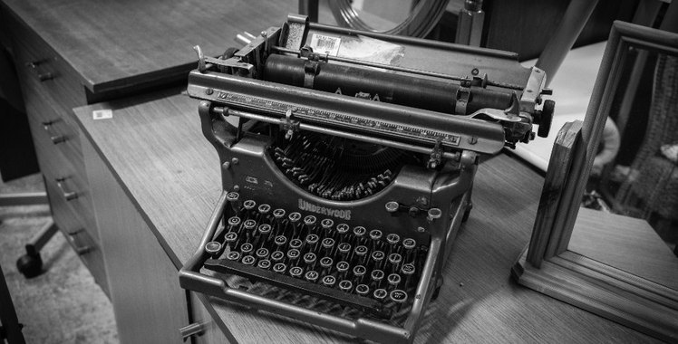 An old manual typewriter standing on a metal desk, black and white